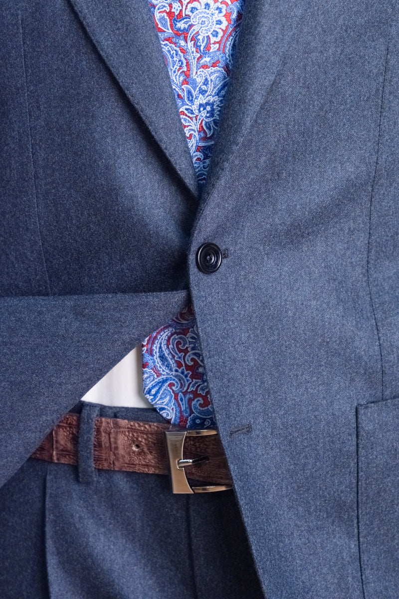 Close-up of a blue suit jacket with a patterned shirt and brown belt.